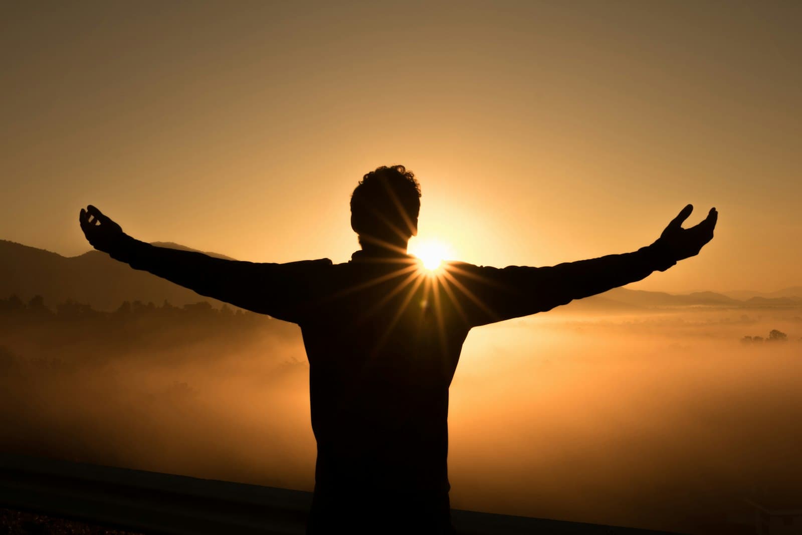 A person above the clouds at sunrise, arm raised